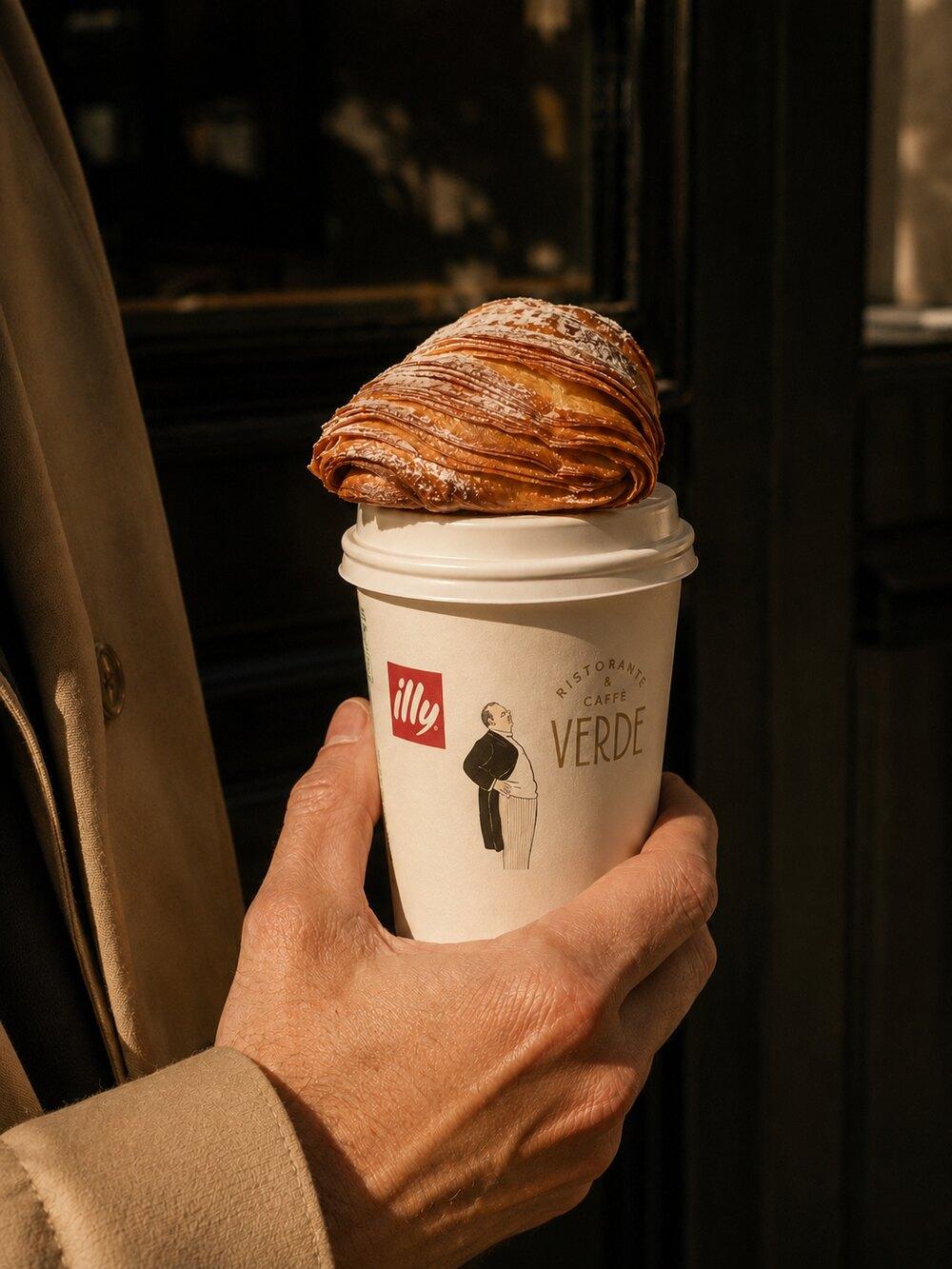 A Verde Caff&egrave; coffee cup topped with a sfogliatella pastry, held on the street