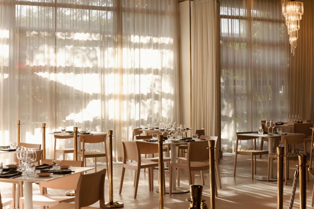The Verde Alexandria dining room in golden afternoon light, sheer curtains and marble tables