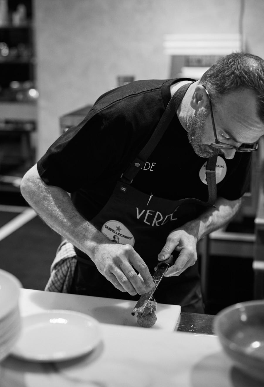 Chef Davide at the pass in the Verde kitchen, grating over a dish in a black Verde apron