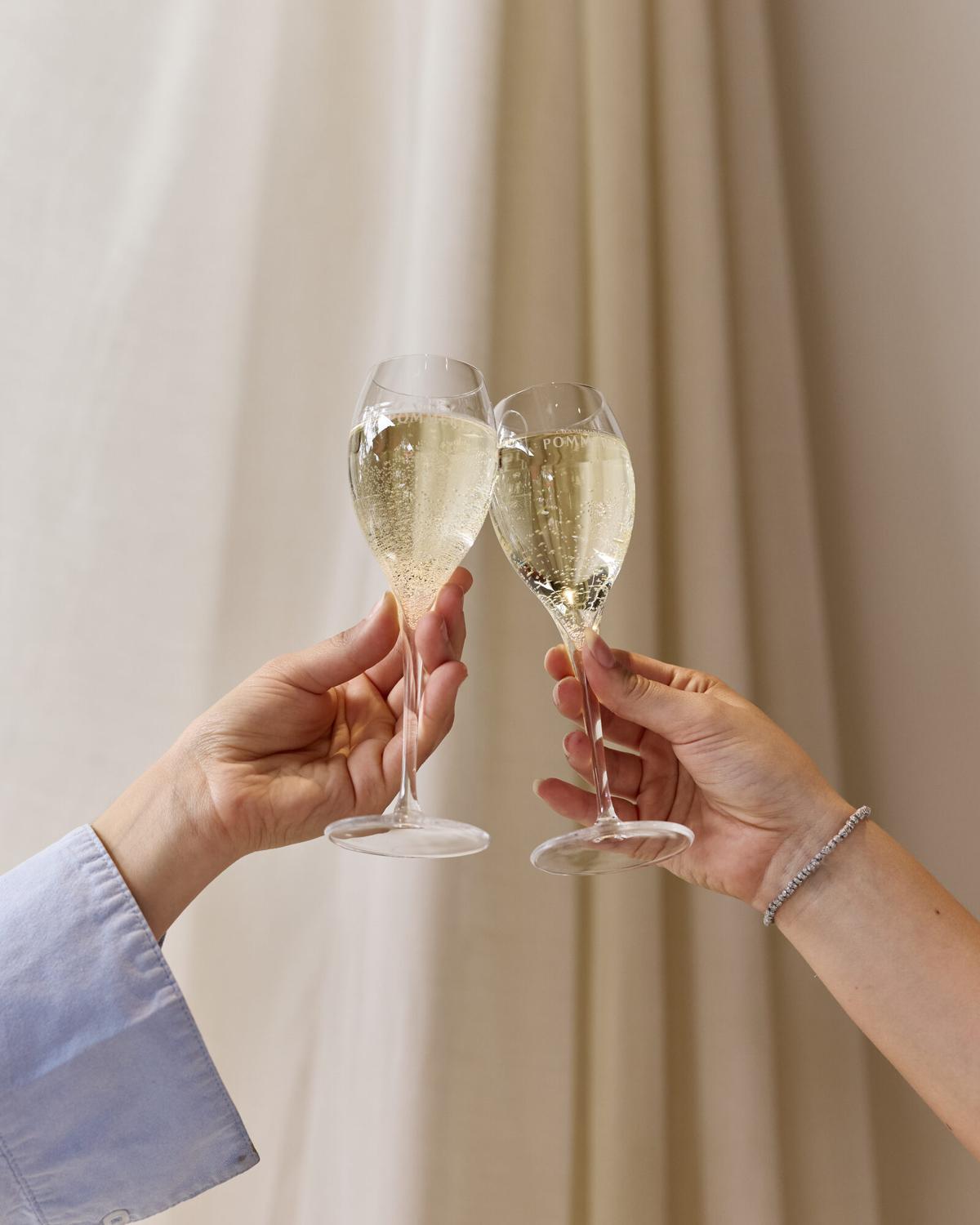 Two guests clinking Pommery champagne glasses in a toast against sheer curtains at a Verde private event